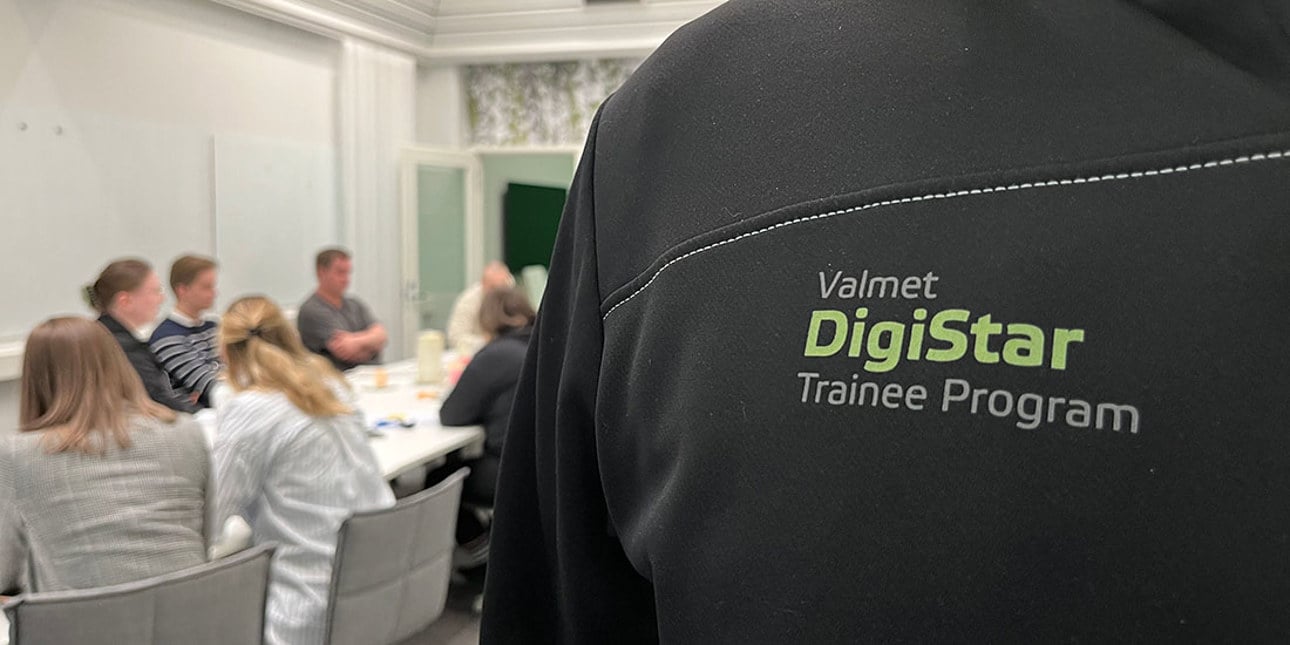 A closeup of a black Valmet DigiStar Trainee Program hoodie and trainees in the background