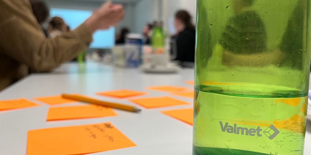 Orange post-it notes and green Valmet water bottle on the table