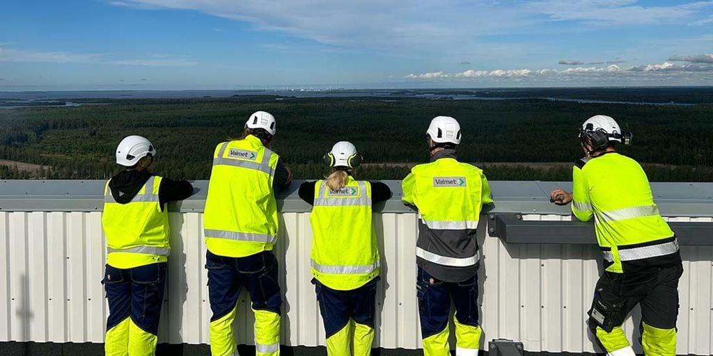 A group of Valmet Project Professional Trainees standing on top of a paper mill looking towards horizon.