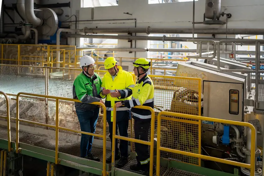 Three men standing in front of a specialty paper machine wet end