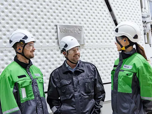 Two Valmet employees discussing with a customer inside a factory. 