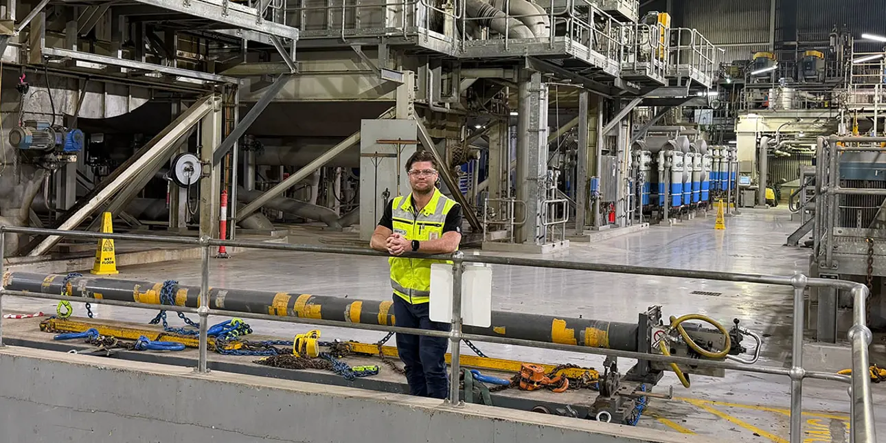 Valmet employee Jack Woodall wearing high-visibility workwear standing inside an industrial facility surrounded by machinery and equipment.